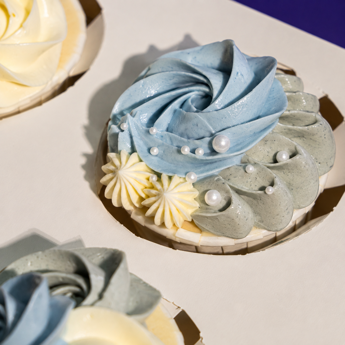 Close-up of a Denim Ruffle cupcake: blue and grey swirls, cream star piping and white sugar pearls