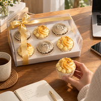 Sunny Swirl cupcake gift box on a work desk beside a notebook and coffee, one cupcake in hand