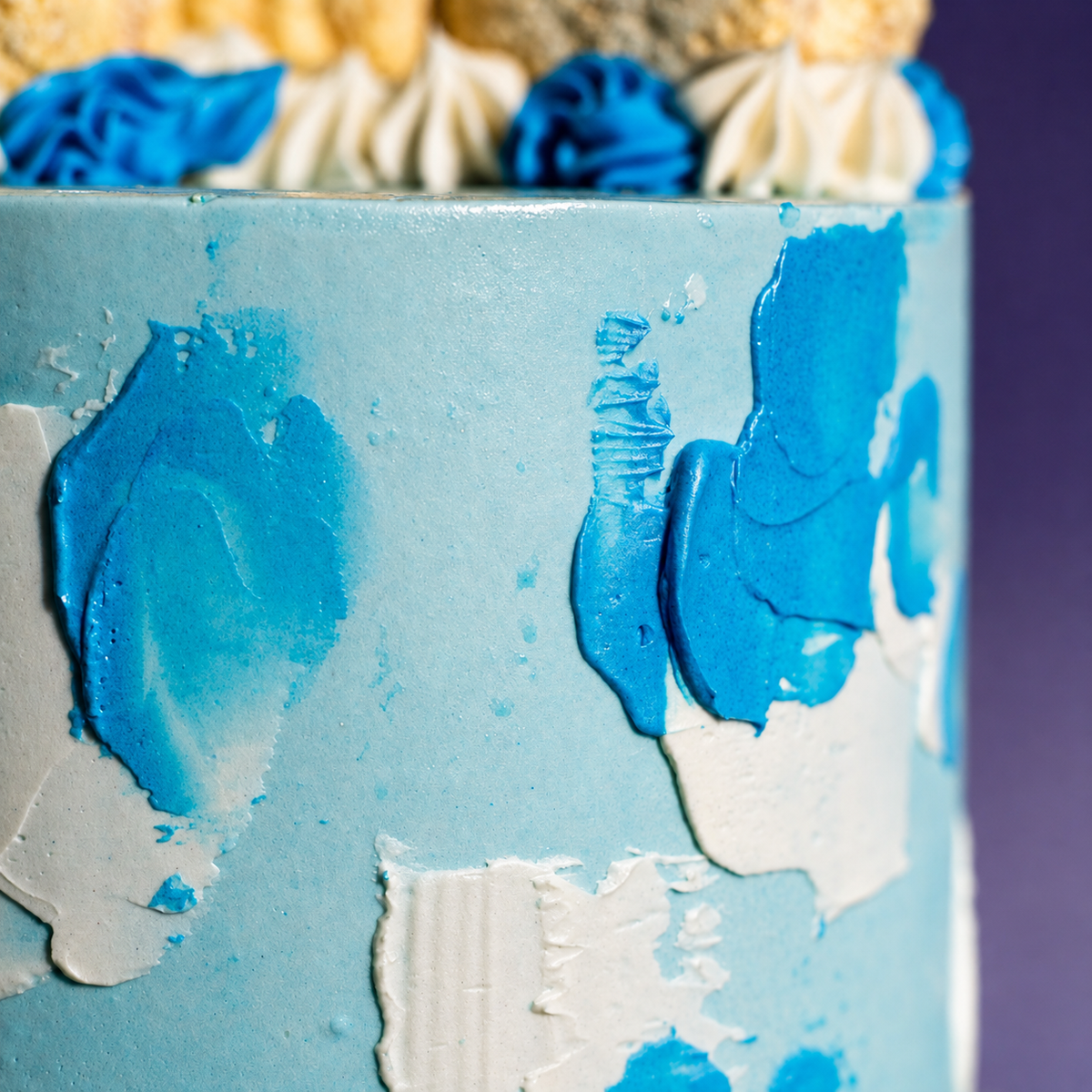 Blue and white piped rosettes and macarons along the top edge of the Brushstroke Blue cake