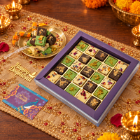 Open gift box of 25 burfi in milk, pistachio and chocolate beside a brass plate of burfi