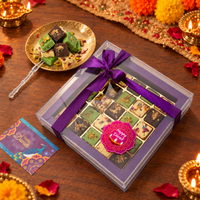Burfi gift box in a clear case tied with purple ribbon, with a plate of burfi beside it