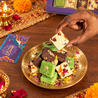 Hand lifting a square of milk burfi from a brass plate