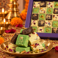 Milk, pistachio and chocolate burfi stacked on a brass plate with the gift box behind