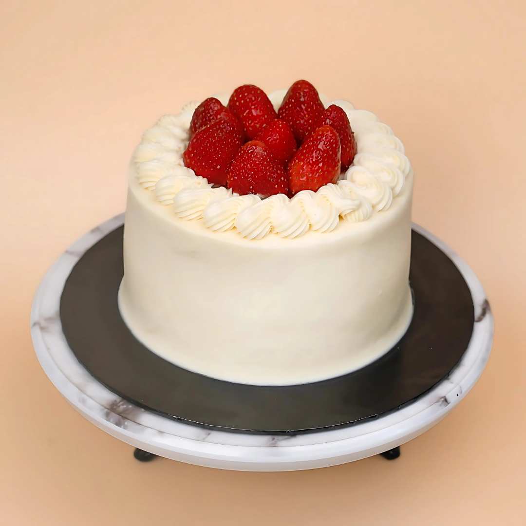 White cake with strawberries on a marble stand against a beige background