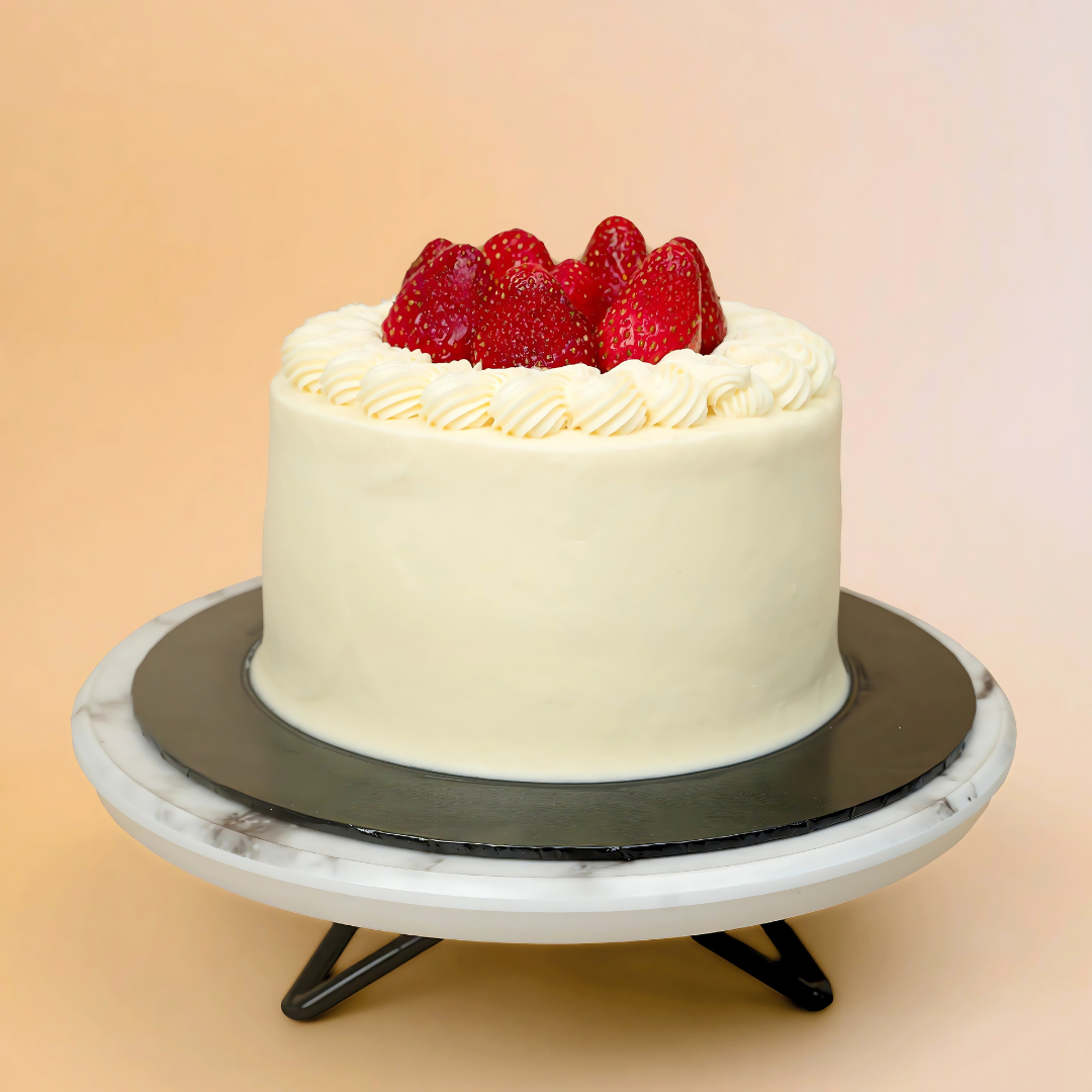 White cake with strawberries on a marble stand against a beige background