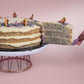 Serving a slice of Lemon Poppyseed cake decorated with poppyseed, dehydrated lemon & rose petals on top by Elevete Patisserie
