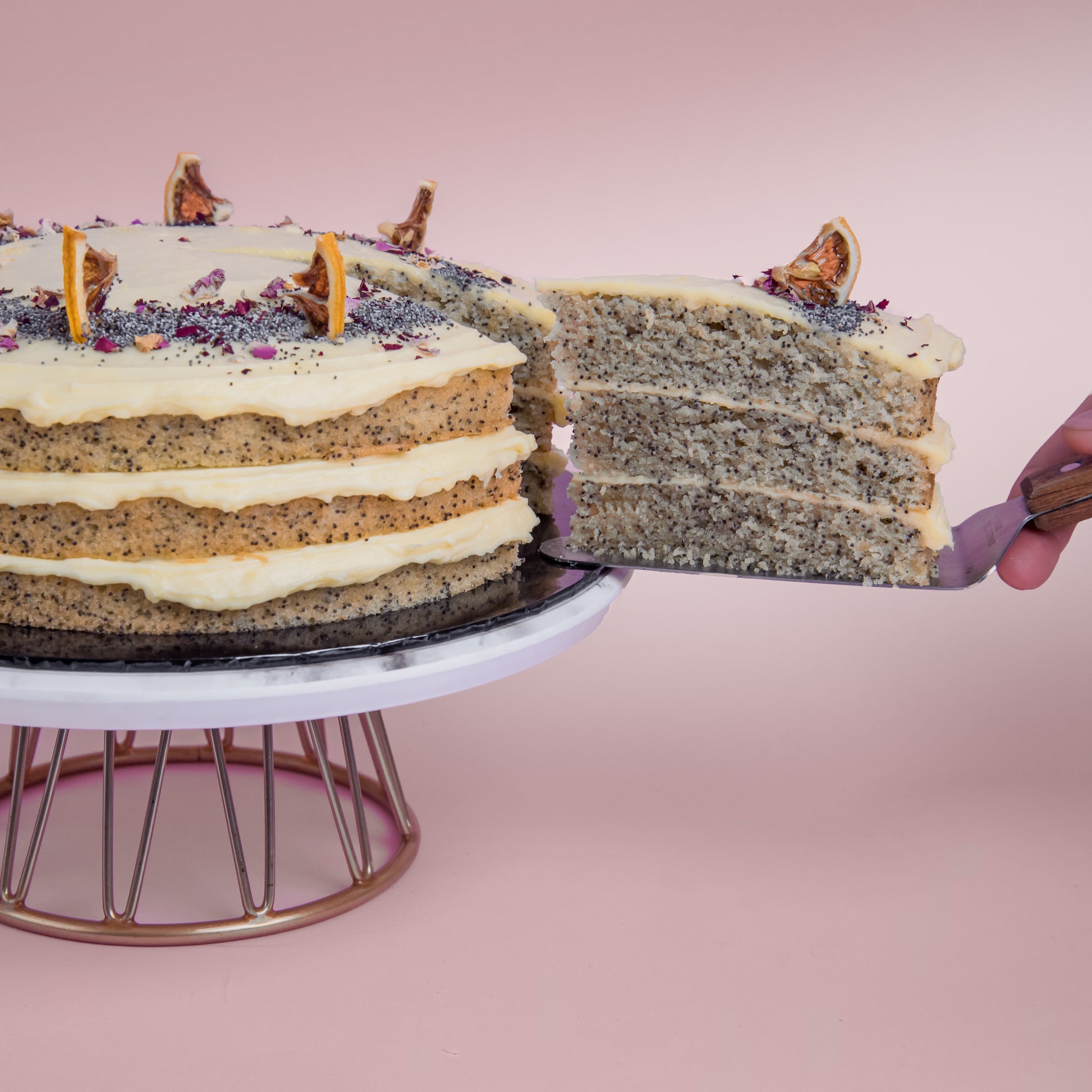 Serving a slice of Lemon Poppyseed cake decorated with poppyseed, dehydrated lemon & rose petals on top by Elevete Patisserie