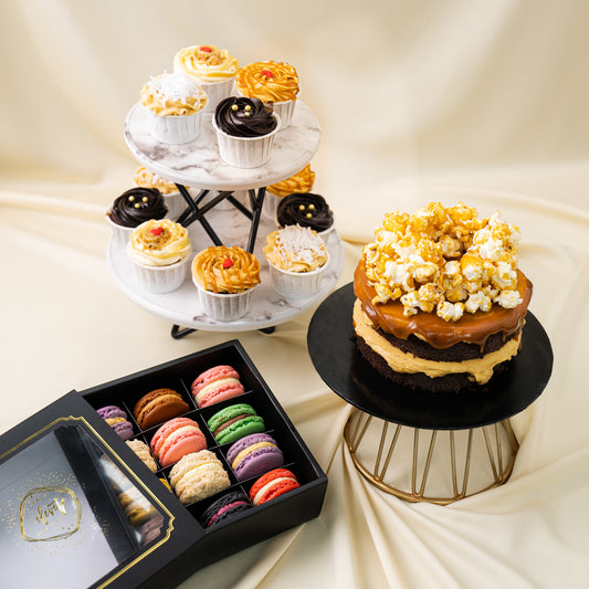 A dessert table including a 5 inch Mini Salted Caramel Chocolate cake with Popcorns on top, a Box of 12 Assorted Macarons & a 12 mixed flavoured cupcakes on a dessert stand