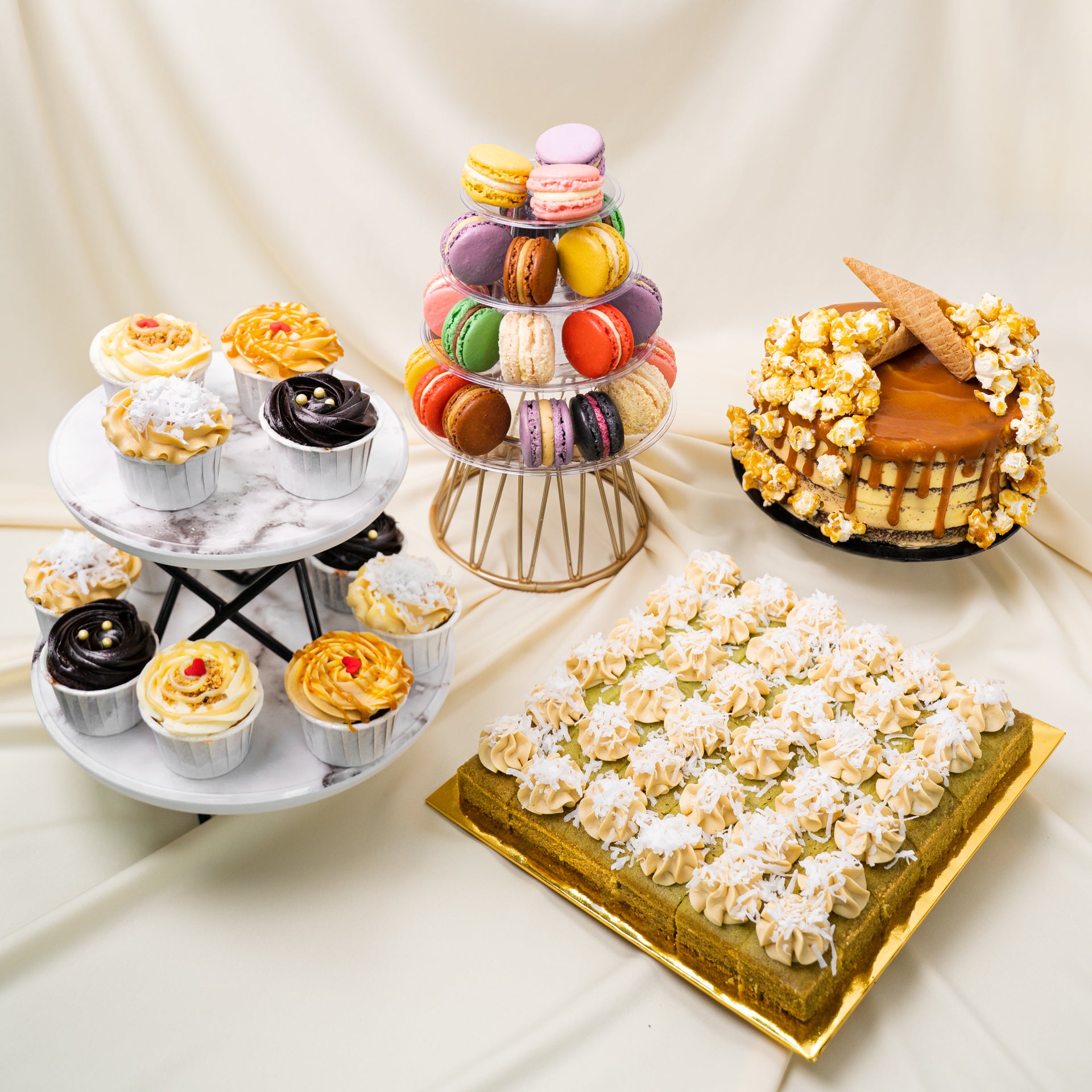 Dessert Table package including a square The Locale Pandan Gula Melaka Cake Cake Bites, 7 inch Signature Popstar Cake, Tower of 25 Assorted Macarons and 12 Mix & Match Cupcakes displayed on a dessert stand